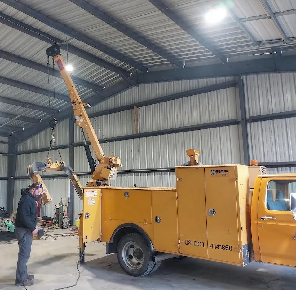 Yellow truck with a crane arm inside a spacious warehouse.